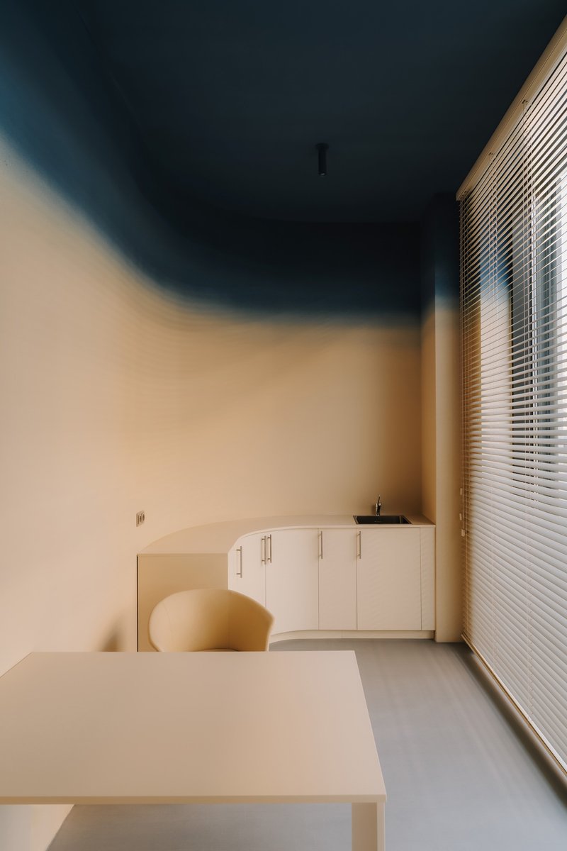 Workroom with pale cabinetry beneath a teal ceiling and horizontal blinds filtering daylight