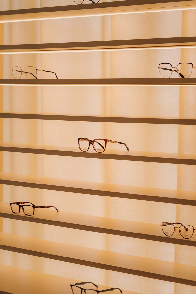Backlit horizontal brass shelving displaying eyeglasses against translucent vertical panels