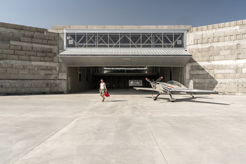 Concrete hangar entrance with stepped retaining walls and figure walking toward parked aircraft on paved apron