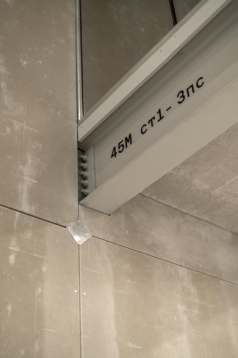 Close-up of white steel frame member with stenciled code marking against concrete panel joint