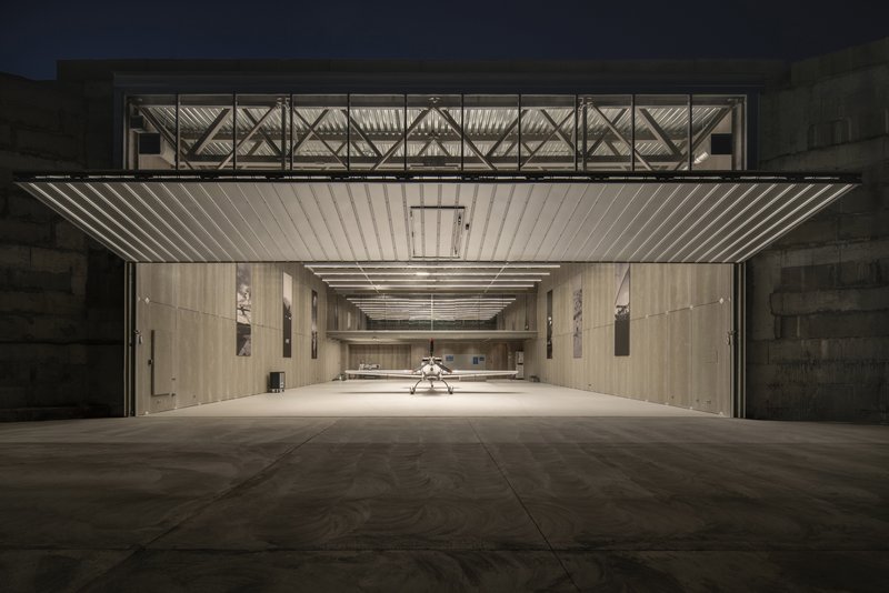 Exterior view of the open hangar door with corrugated metal soffit and exposed truss structure at dusk