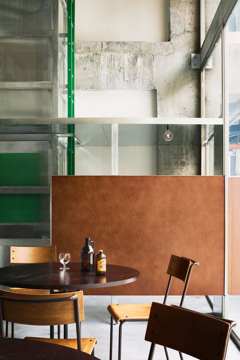 Seating area with copper partition panel against exposed concrete walls and green-framed translucent glass doors