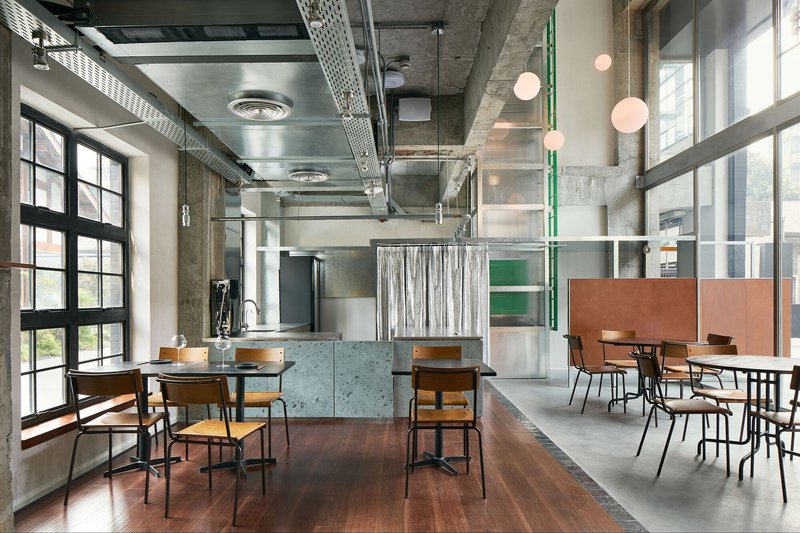 Interior dining space with exposed concrete ceiling, ventilation ducts, and pink globe pendant lights