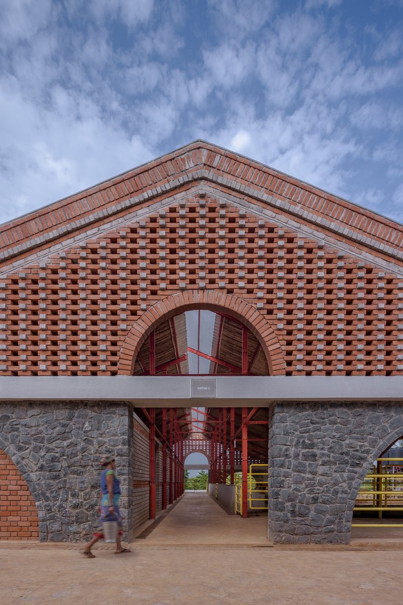 Gabled brick facade with chequered brickwork and arched opening with red metal gates under a cloudy sky