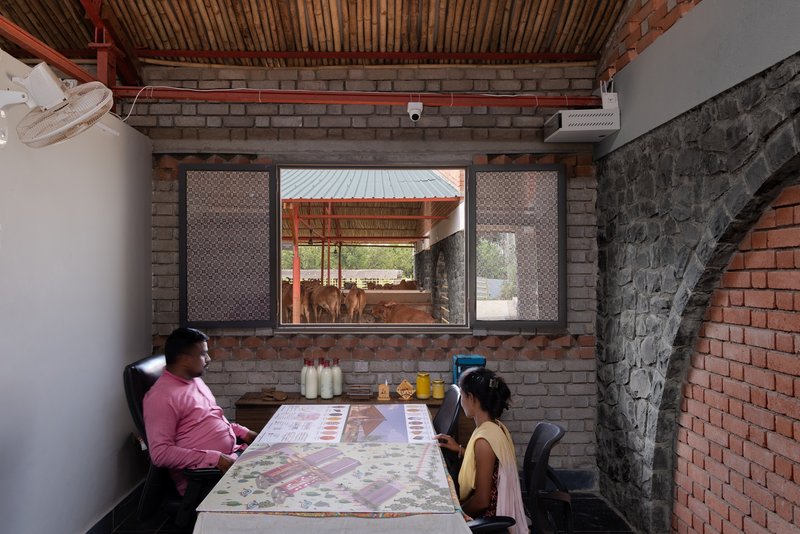 Office interior with two people at a table framed by perforated brick screens overlooking the cattle enclosure