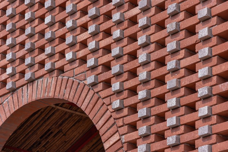 Patterned brick wall with alternating red and grey units forming a basketweave texture around an arched opening