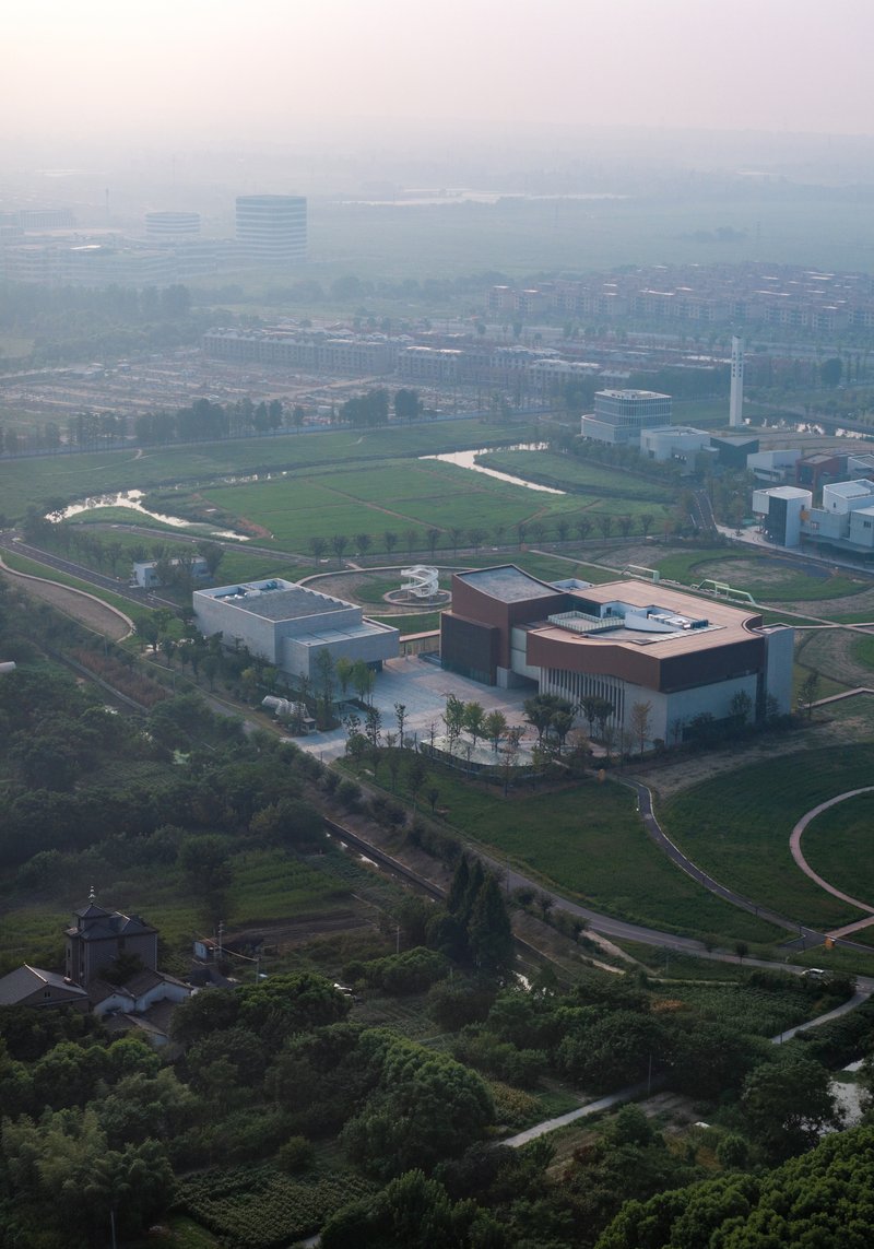 Aerial view of two connected volumes surrounded by green fields and agricultural landscape in morning haze