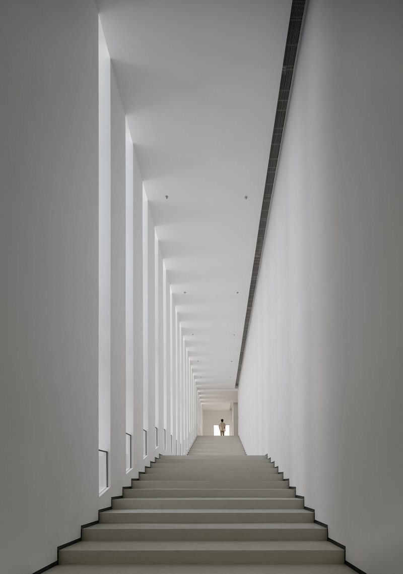 White staircase flanked by vertical columns of daylight with two figures silhouetted at the top
