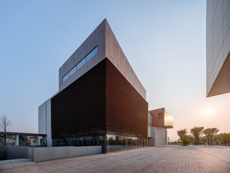 Corner view showing the horizontal bronze louver volume cantilevered above the concrete base at dusk
