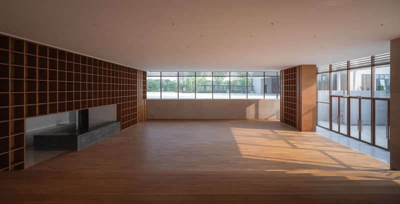 Open-plan interior with timber shelving grid, stone floor and ribbon windows overlooking a terrace
