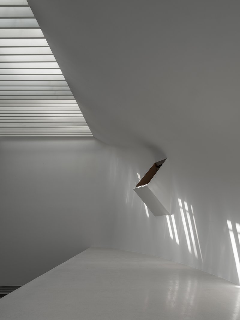 White interior staircase with timber handrail catching striped shadows from overhead louvers