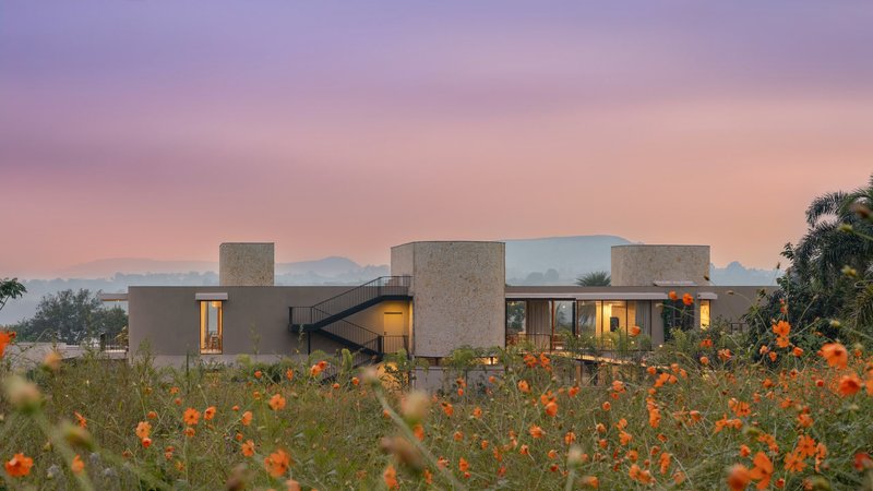 Stone-clad volumes with glazed openings and exterior stair framed by orange flowers under a pink sunset sky