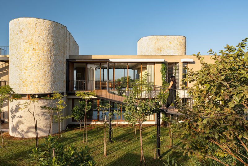 Two-level facade with stone cylindrical towers, timber-framed glazing, and metal balustrades overlooking a lawn