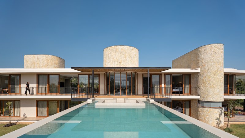 Rear elevation with three cylindrical stone towers flanking a glazed living volume and terrace over a reflecting pool
