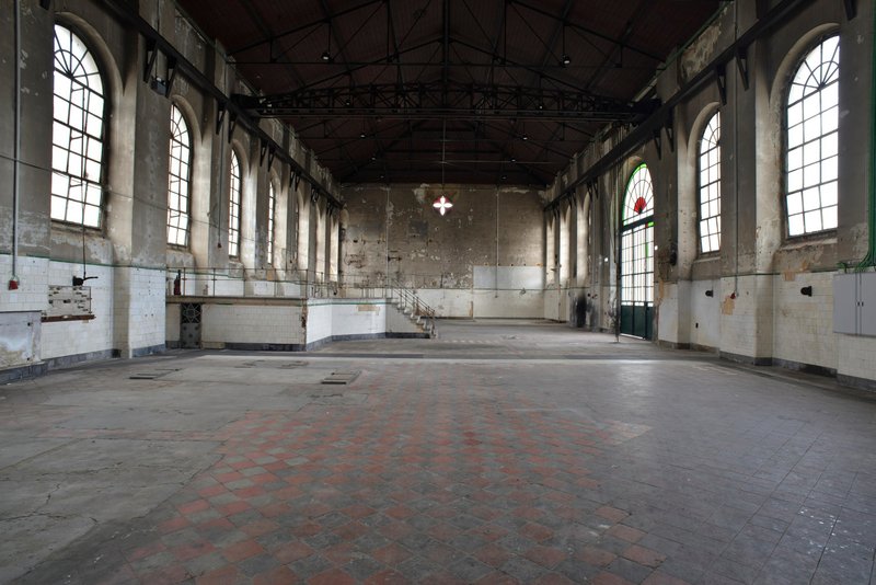 Empty interior hall with exposed concrete walls and arched windows before renovation