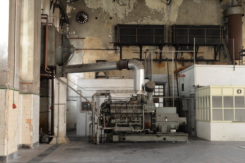 Interior view of an industrial space with exposed machinery, galvanized ductwork, and weathered concrete walls