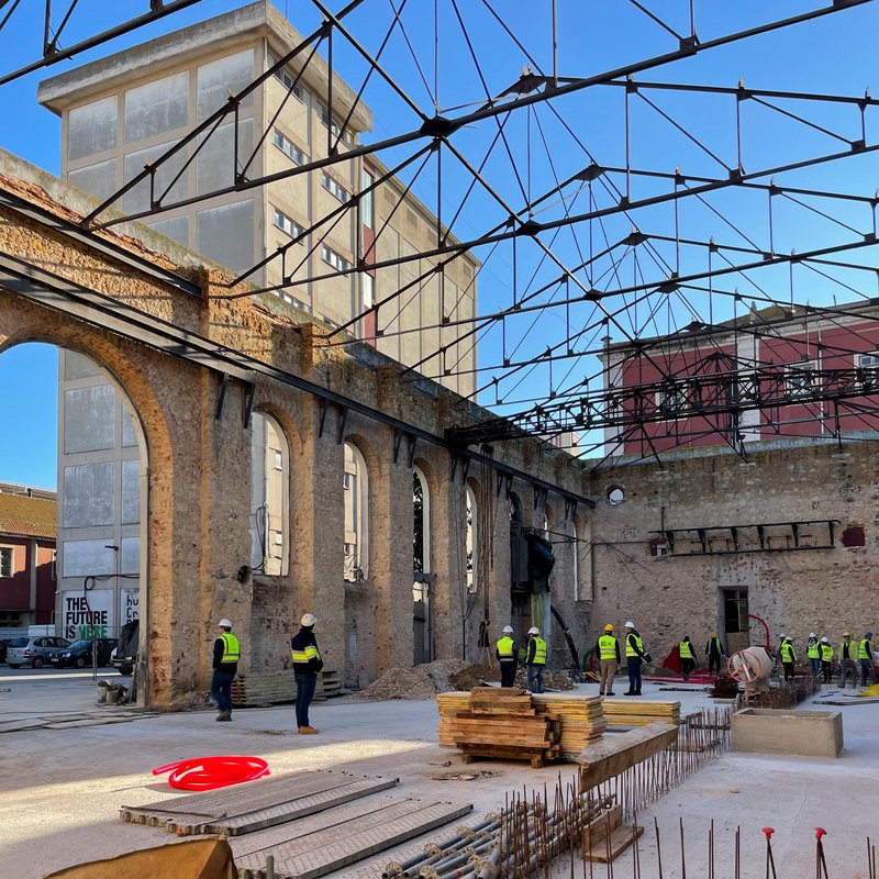 Arched stone facade beneath a new steel truss roof during construction with workers in high-visibility vests