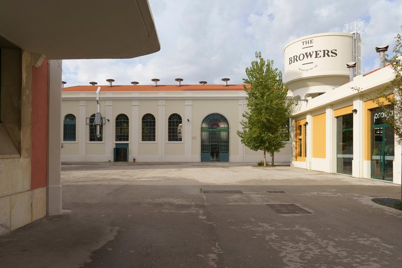 Courtyard with white masonry buildings flanking a central tree under partly cloudy skies