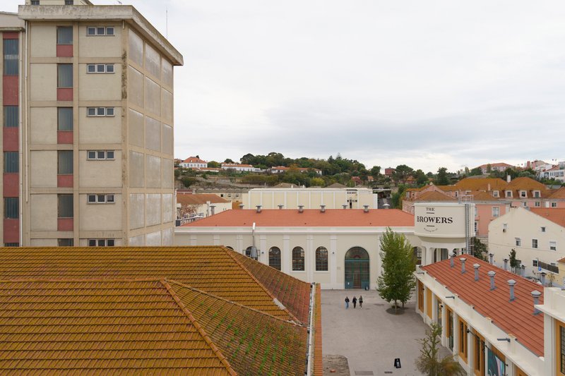 Rooftop view of a public square with a white arcaded facade and three figures walking below