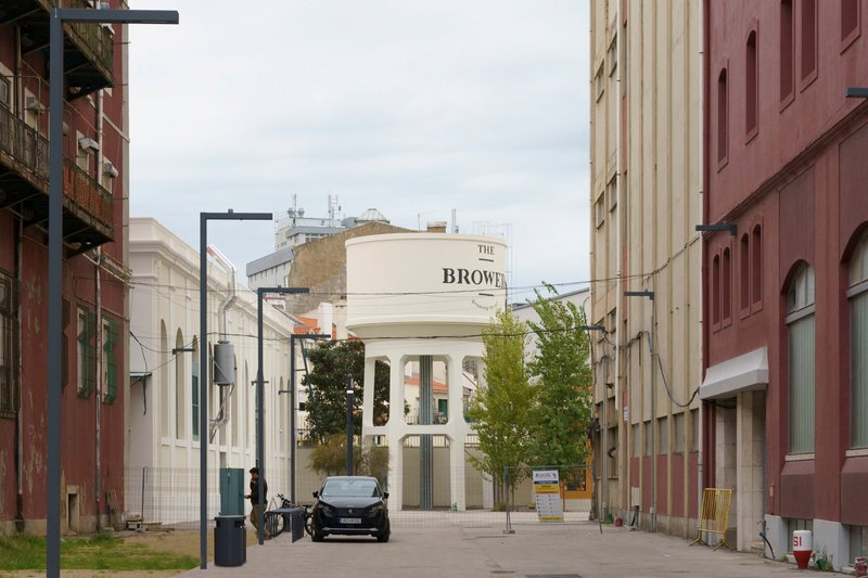 Pedestrian plaza framed by industrial buildings with a cylindrical water tower in the distance