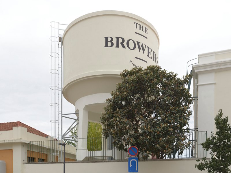 Cylindrical water tower with signage partially obscured by a mature tree in the foreground