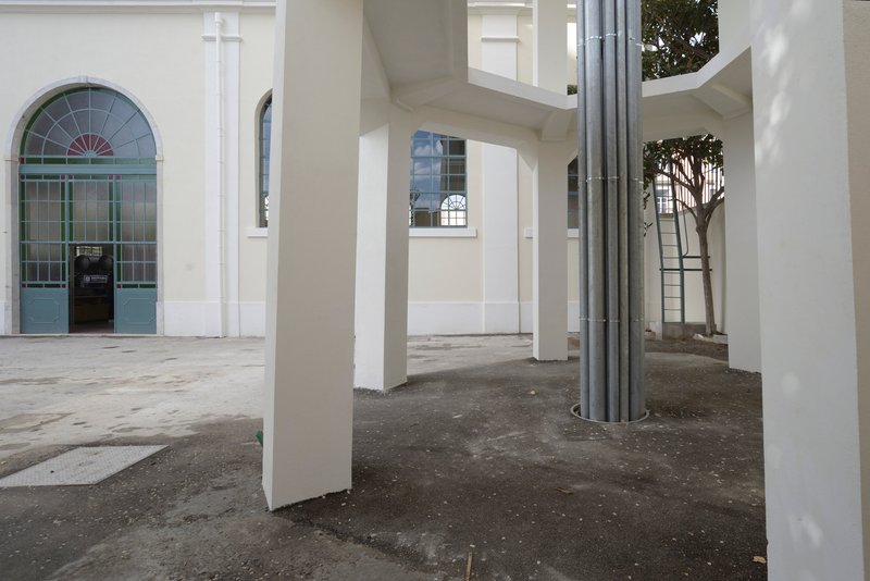 Covered arcade with white square columns and a circular metal duct wrapping around one pillar