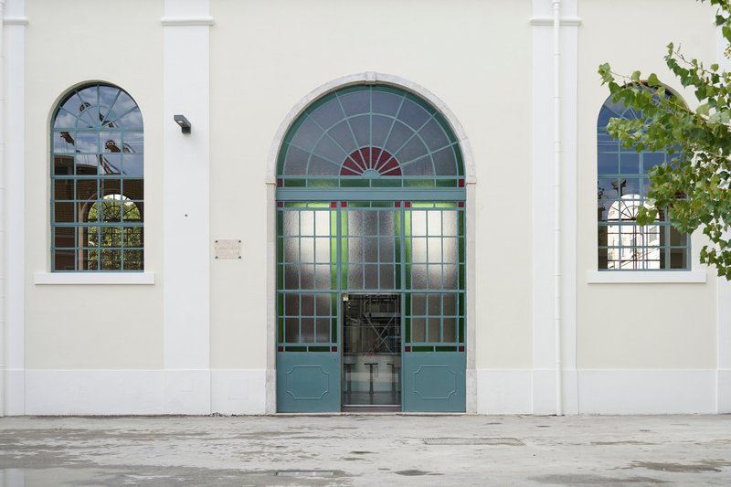 Street view of the arched entrance with grey-green steel and glass double doors flanked by arched windows