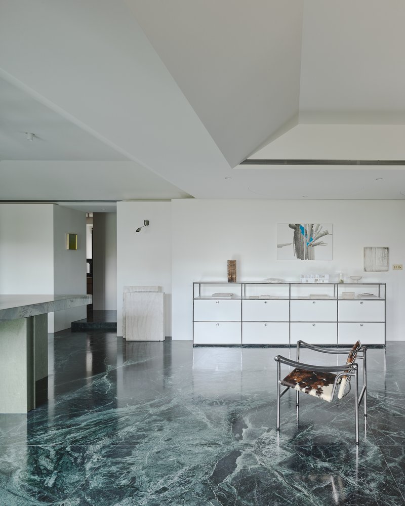 This architectural image showcases a modern and minimalist living room with a striking green marble floor. The space features white walls, a geometric ceiling,
