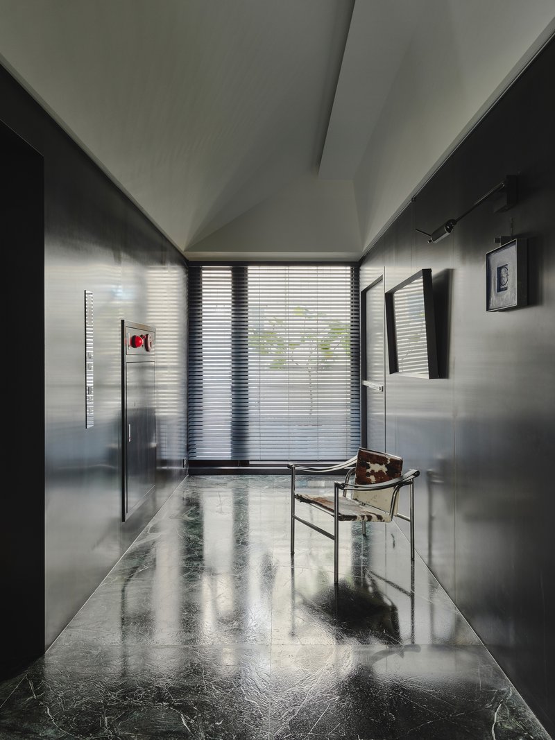 This architectural image showcases a modern hallway with a minimalist design. The space features polished marble floors, metal paneling, and a geometric ceiling