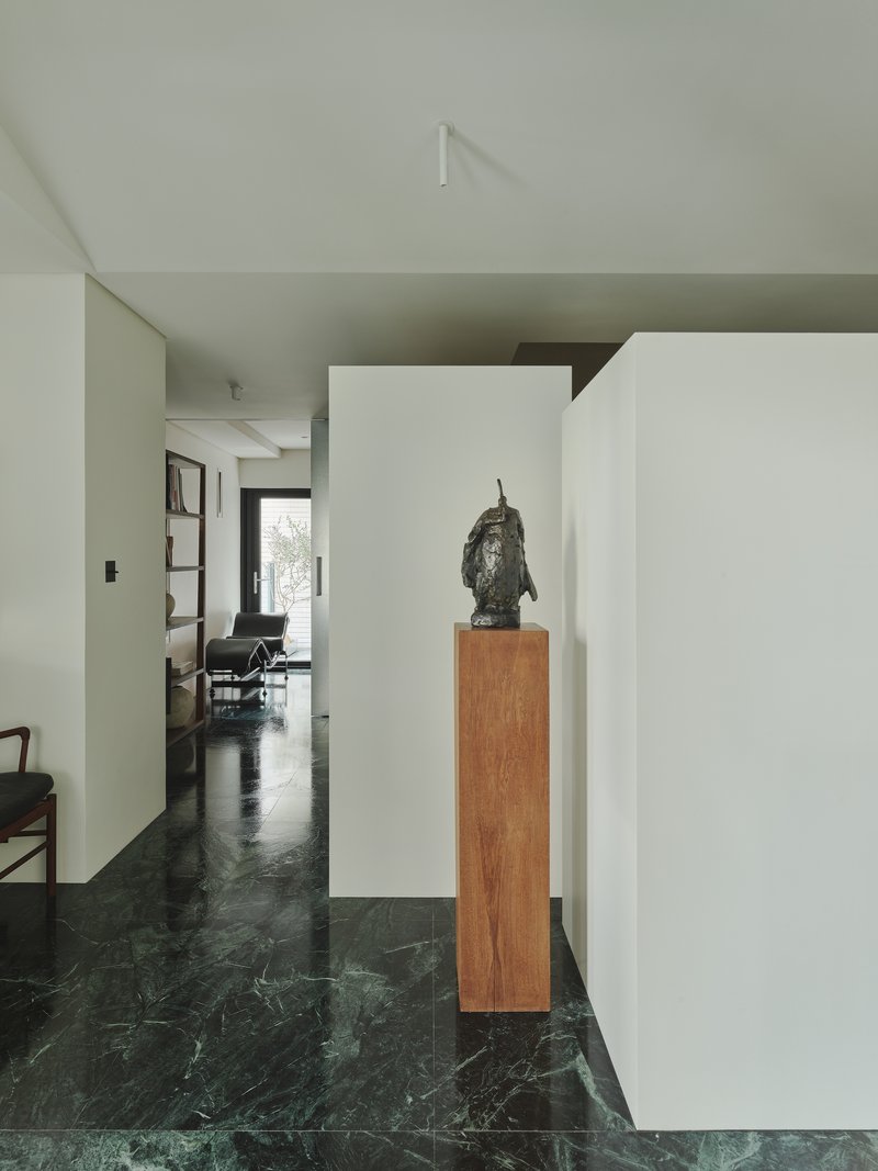 This architectural image showcases a modern interior with a minimalist design. The space features a hallway with green marble flooring, white walls, and a sculp