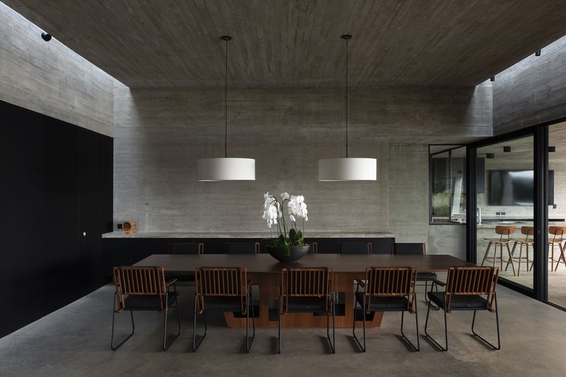 Dining room with boardmarked concrete ceiling and walls flanking a long table under pendant lights