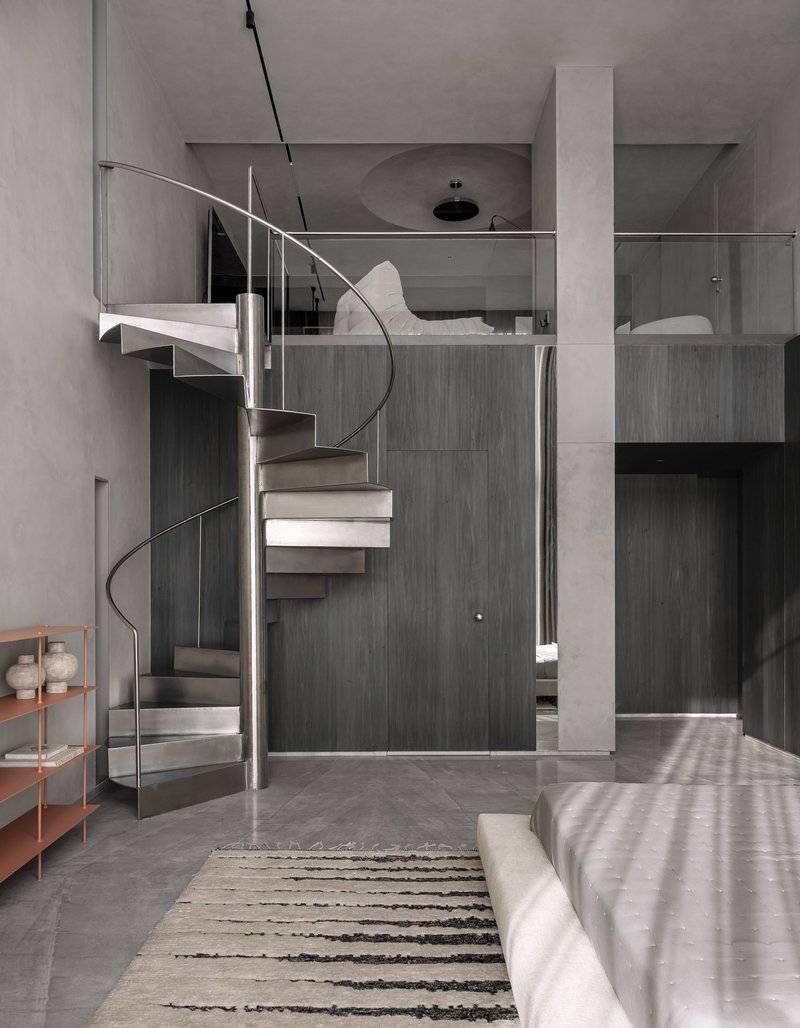 Steel spiral staircase connecting lower bedroom to mezzanine level beneath diffused daylight