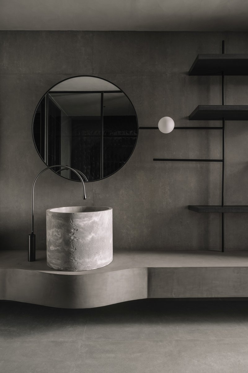 Bathroom vanity detail with cylindrical white stone basin and circular mirror against concrete wall