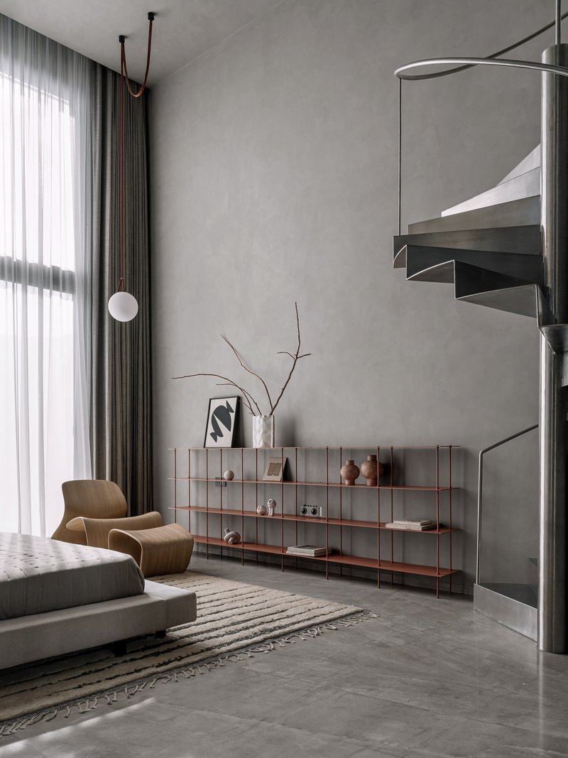 Steel spiral staircase with floating treads beside low shelving unit and grey curtain wall