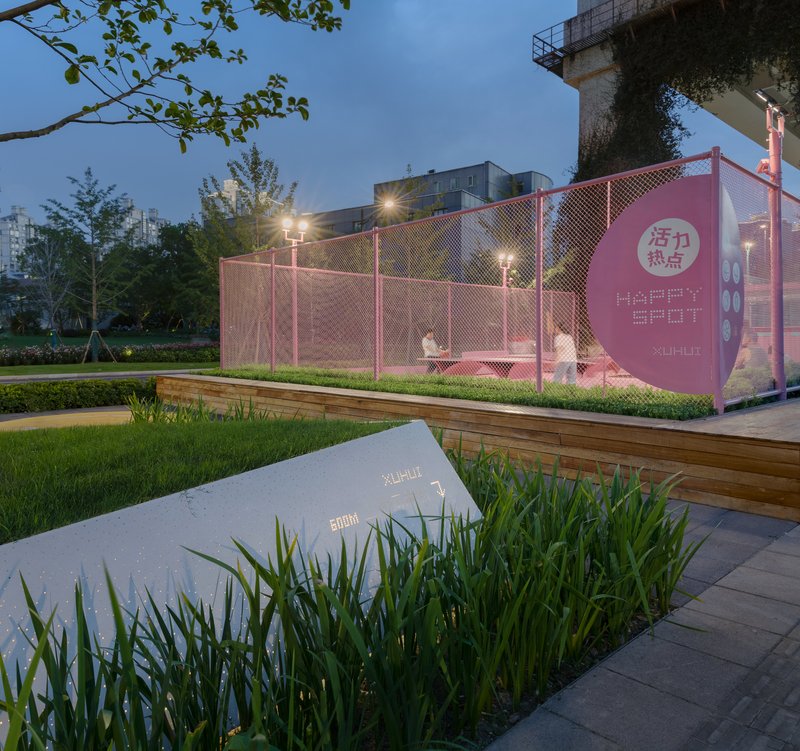 Pink mesh-fenced court beneath a concrete overpass lit by evening light with planted borders