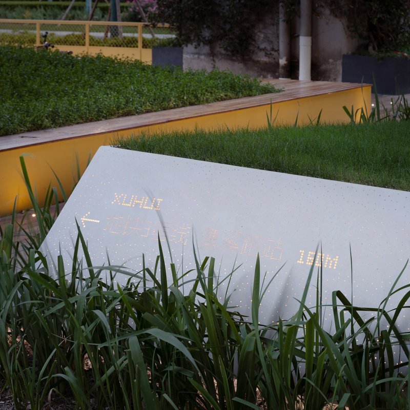 Perforated white panel with interior lighting surrounded by tall grasses at dusk