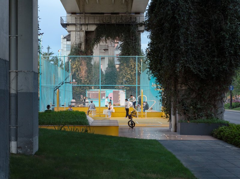 Basketball court under an elevated concrete structure with people playing at twilight