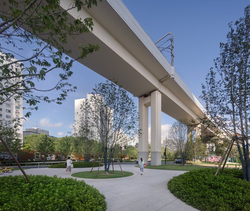 Elevated rail viaduct supported by concrete columns in a landscaped park with walking paths