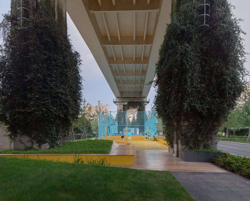Underside of concrete bridge deck framing lawn and timber pathway between vine-covered support columns at dusk