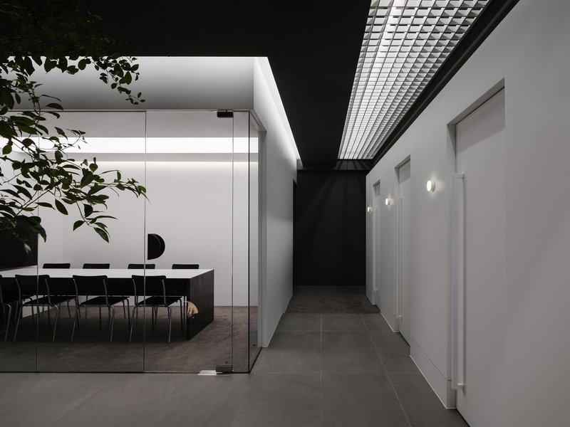 Hallway view toward a glass-enclosed conference room with a metal mesh ceiling panel above