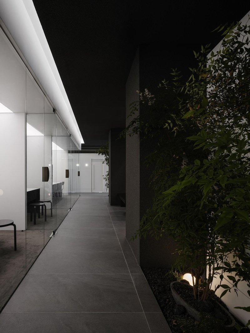 Evening corridor with uplights illuminating a planted green wall and a glazed office beyond