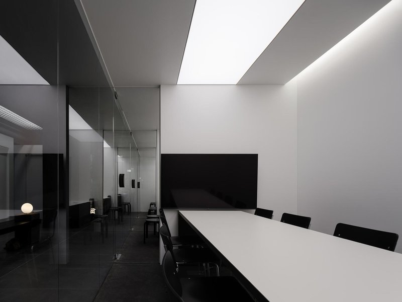 Conference room with white table and recessed linear skylights casting angular shadows on the ceiling