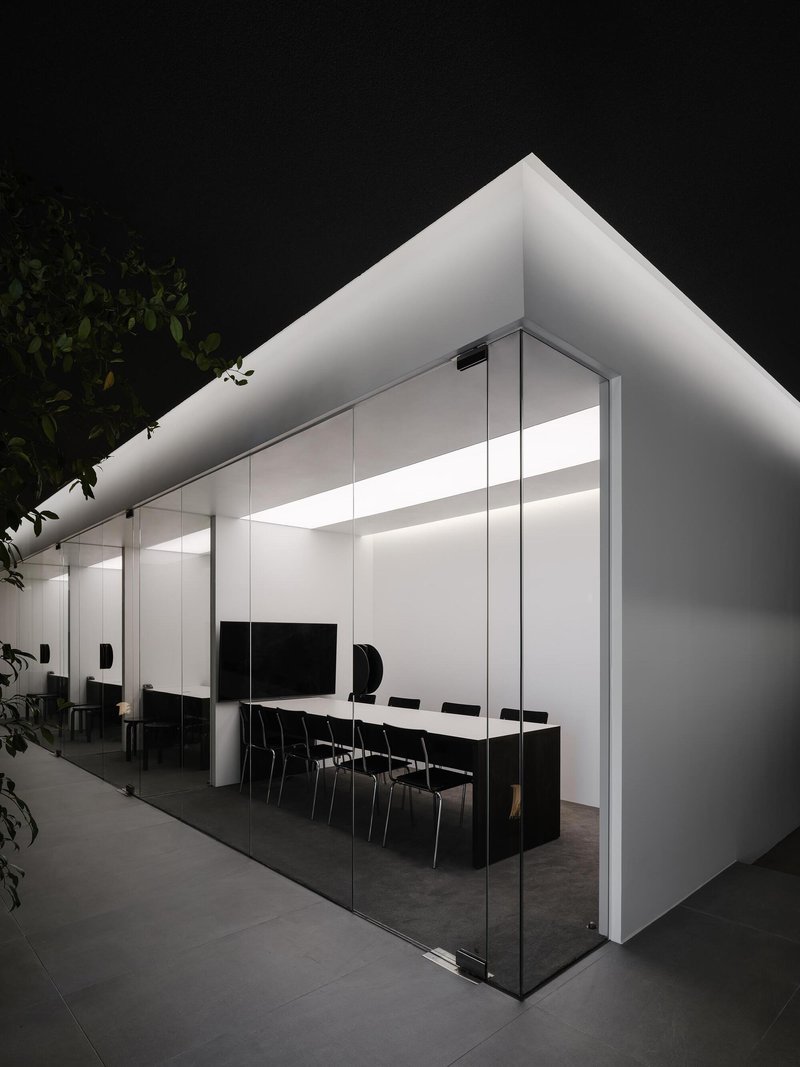 Glass-enclosed meeting room volume with continuous perimeter lighting glowing against the night sky