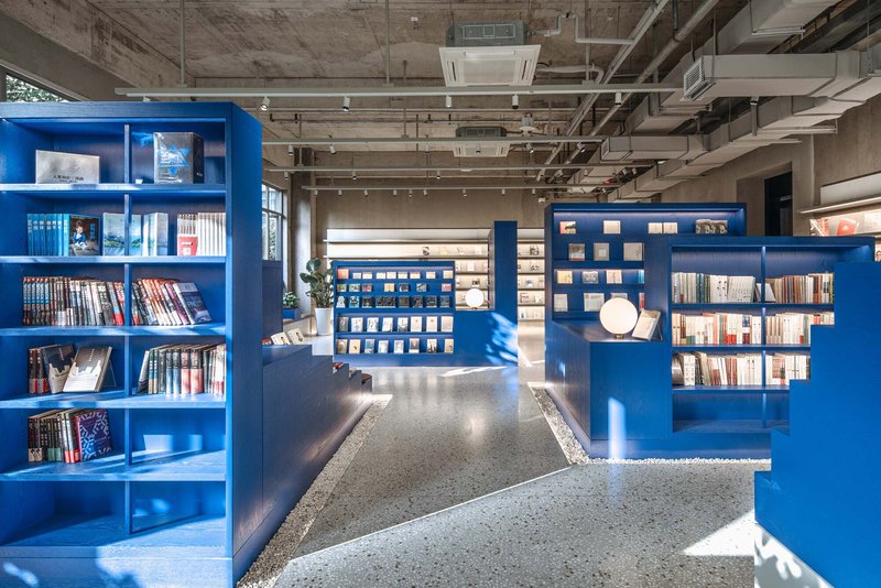 Interior bookstore with blue freestanding shelving units and exposed concrete ceiling with visible mechanical systems