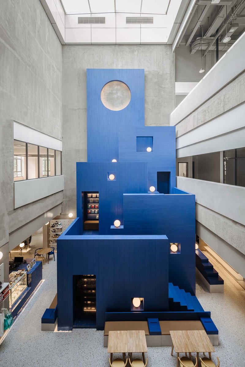 Multi-story atrium with a stepped blue staircase structure under a skylight with concrete balconies
