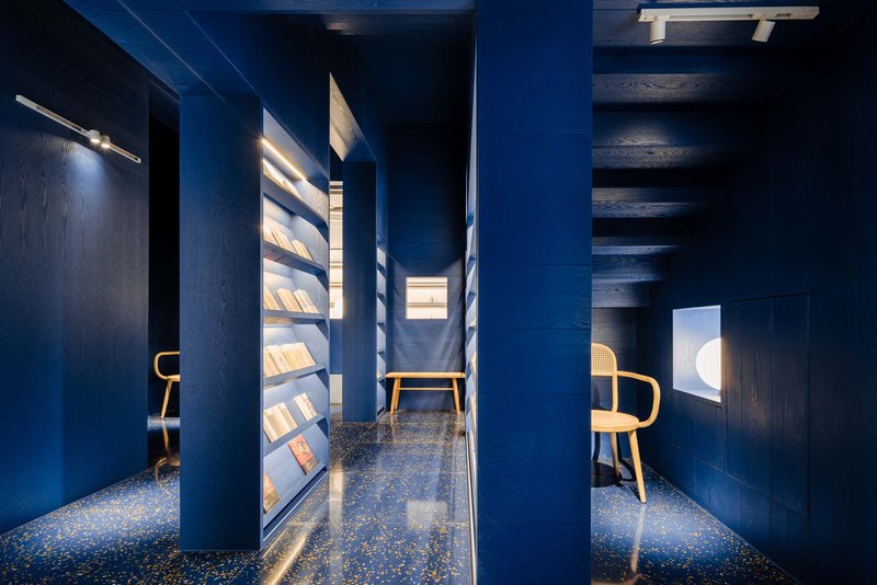 Narrow reading corridor with blue walls, illuminated book display shelves, and terrazzo flooring