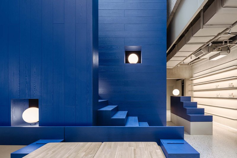 Blue timber-clad wall with integrated staircase and circular porthole lights beside white bookshelves