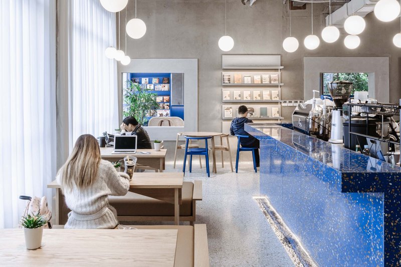 Cafe interior with blue terrazzo counter, white globe pendants, and patrons at timber tables