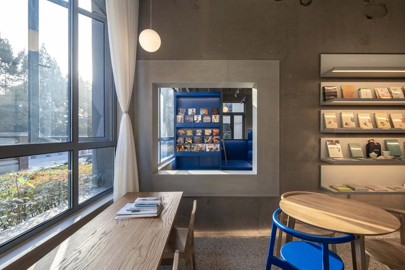 Reading nook with timber bench, framed window into blue bookshop, and garden view beyond