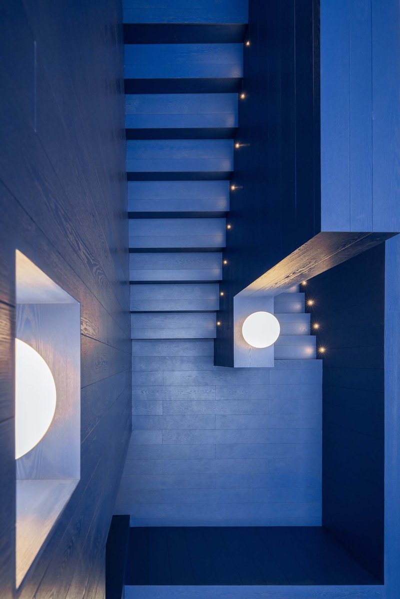 Top-down view of a suspended staircase with illuminated treads and circular ceiling openings at dusk